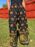 Person wearing black Boho-style straight pants with colorful elephant patterns in a grassy area.